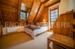 Cozy chalet bedroom with wooden walls and ceilings, featuring a comfortable double bed and a charming wicker chair.