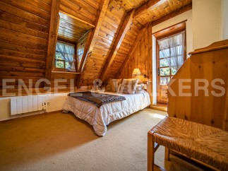Cozy chalet bedroom with wooden walls and ceilings, featuring a comfortable double bed and a charming wicker chair.