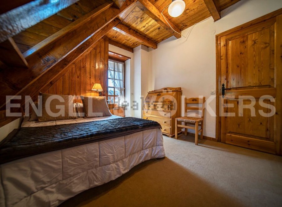 Cozy chalet bedroom with wooden beams and walls, featuring a comfortable double bed and a charming wooden secretary.