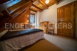 Cozy chalet bedroom with wooden beams and walls, featuring a comfortable double bed and a charming wooden secretary.