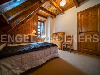 Cozy chalet bedroom with wooden beams and walls, featuring a comfortable double bed and a charming wooden secretary.