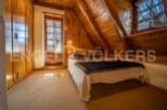 Cozy attic bedroom with wooden walls and beams, featuring a comfortable bed and built-in wardrobe.