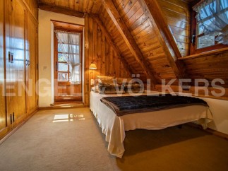 Cozy attic bedroom with wooden walls and beams, featuring a comfortable bed and built-in wardrobe.