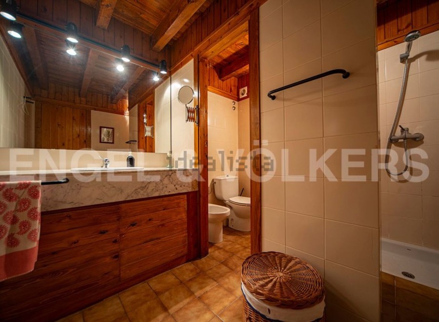 This charming bathroom boasts a rustic wooden vanity with marble countertop, complemented by warm lighting and a spacious mirror.