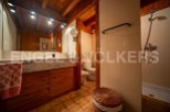 This charming bathroom boasts a rustic wooden vanity with marble countertop, complemented by warm lighting and a spacious mirror.