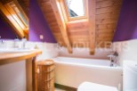 Charming attic bathroom with wooden beams, skylight, and purple walls.