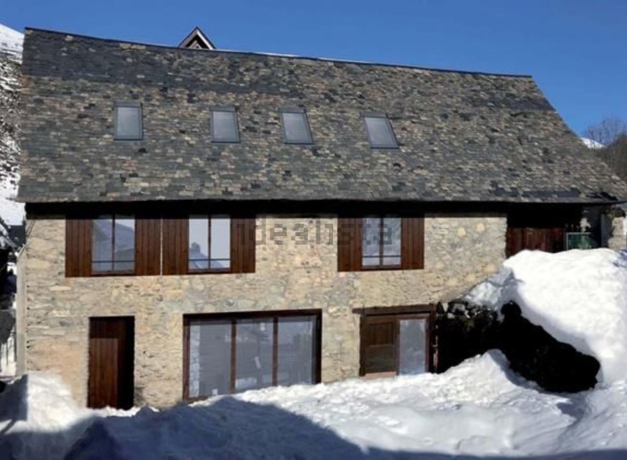 This charming stone house boasts a slate roof, large windows, and a rustic wooden door.