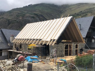 Mountainside home under construction boasts a unique A-frame design and stone exterior.