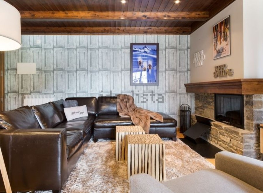 Cozy mountain chalet with leather sectional sofa, stone fireplace, and wood-paneled ceiling.