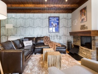 Cozy mountain chalet with leather sectional sofa, stone fireplace, and wood-paneled ceiling.