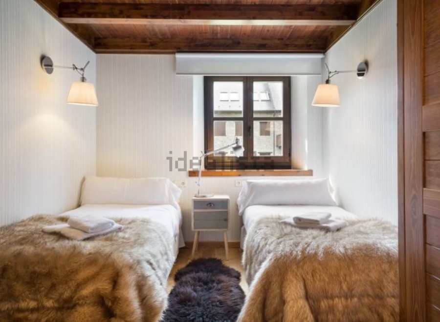 Cozy twin bedroom with rustic wooden beams and a charming window overlooking the town.