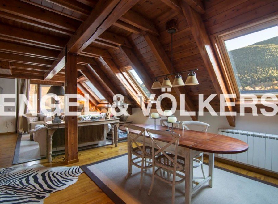 This stunning attic apartment boasts a spacious open-plan living area with exposed wooden beams and large skylights, creating a bright and airy atmosphere.