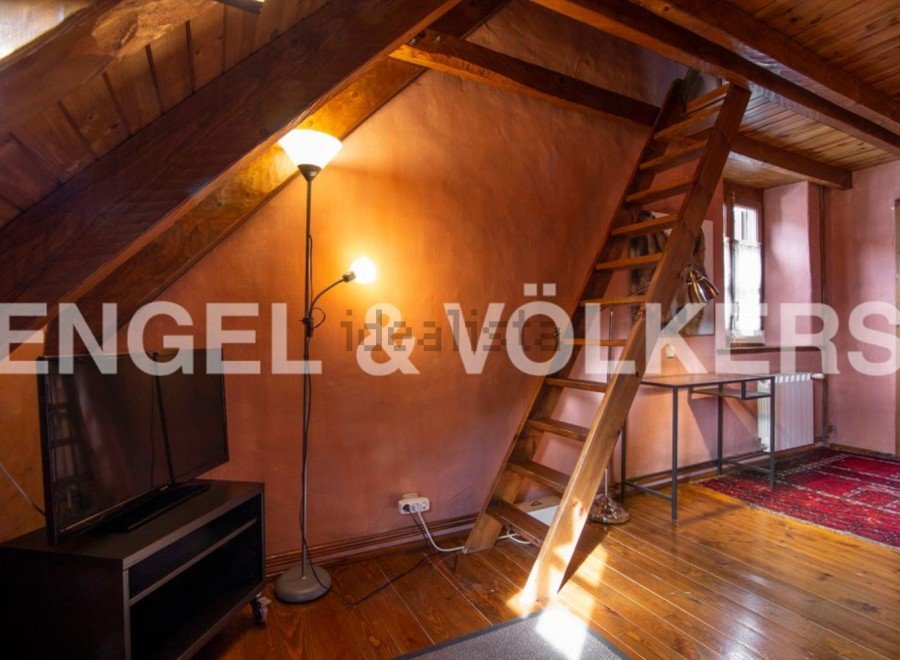 Charming attic room with wooden beams, exposed brick walls, and a wooden ladder leading to a loft.