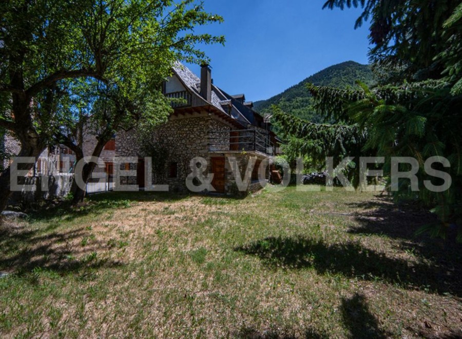 Mountainside stone house with large grassy yard and mountain views.