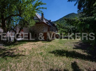 Mountainside stone house with large grassy yard and mountain views.