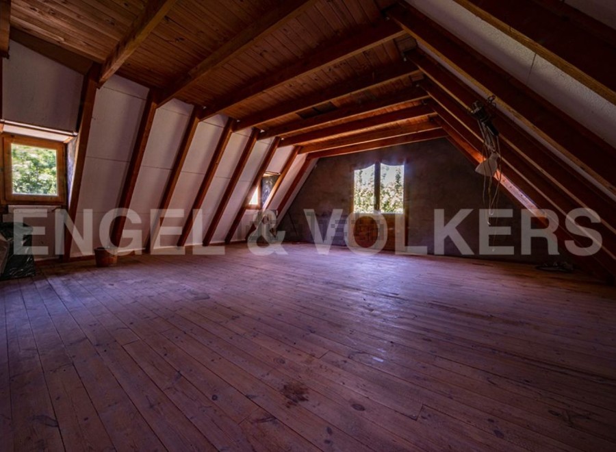 Spacious attic room with wooden beams and flooring, offering ample storage or living space.