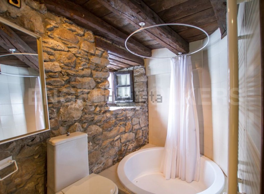 Rustic bathroom with stone walls and wooden beams.