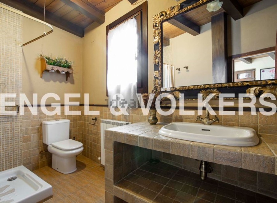 Rustic bathroom with tiled walls and floors, featuring a toilet, shower, and ornate sink vanity.