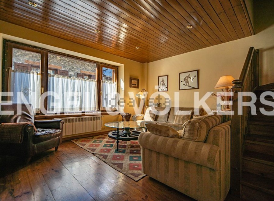 Cozy living room with wooden floors and beamed ceiling, featuring a large bay window and comfortable seating.