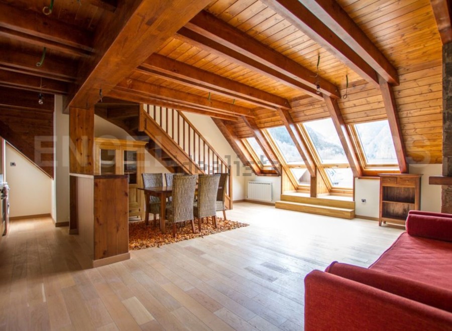 This stunning chalet boasts a spacious open-plan living area with exposed wooden beams and large skylights, creating a bright and airy atmosphere.