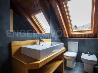 Charming attic bathroom with wooden beams, skylights, and dark slate tiles.