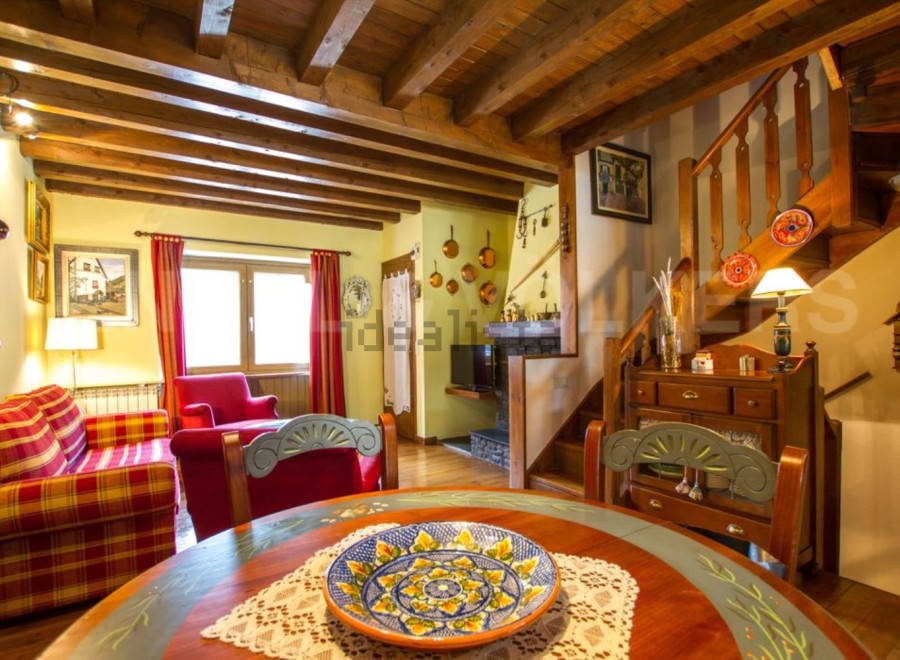 Charming rustic apartment with exposed wooden beams, a cozy living area featuring a plaid sofa and armchair, and a quaint dining space.