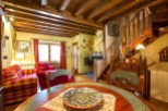 Charming rustic apartment with exposed wooden beams, a cozy living area featuring a plaid sofa and armchair, and a quaint dining space.