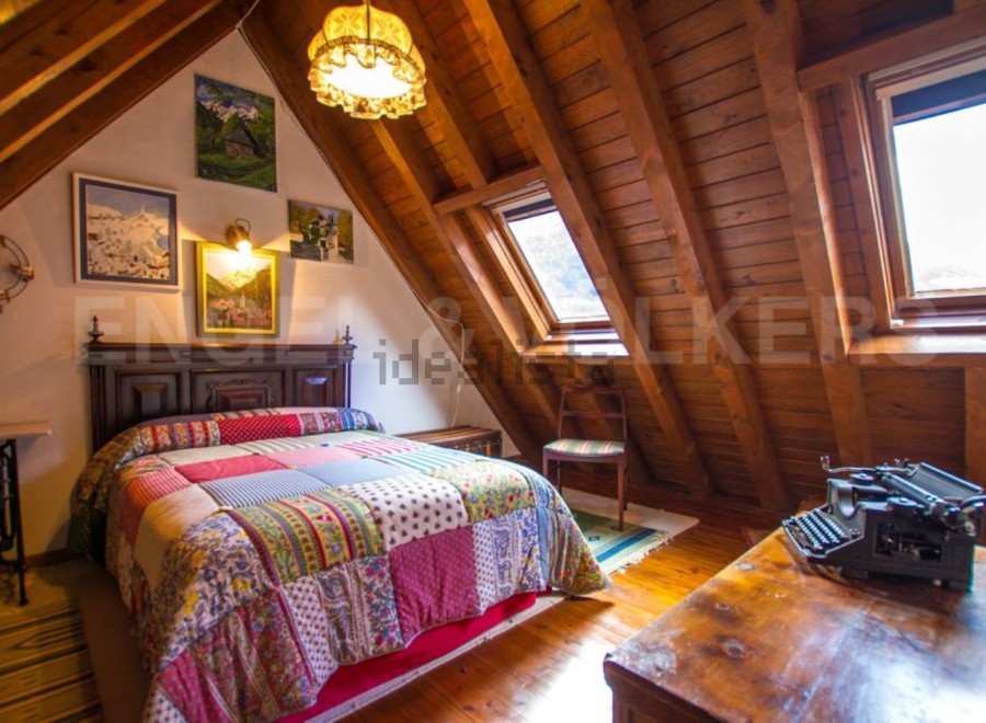 Charming attic bedroom with wooden beams, skylights, and patchwork quilt.