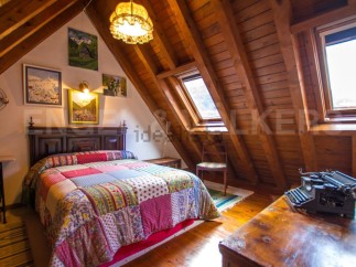 Charming attic bedroom with wooden beams, skylights, and patchwork quilt.