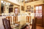 Charming dining room with a glass-top table and wooden chairs, complemented by a large ornate mirror reflecting the kitchen and a beautiful chandelier.