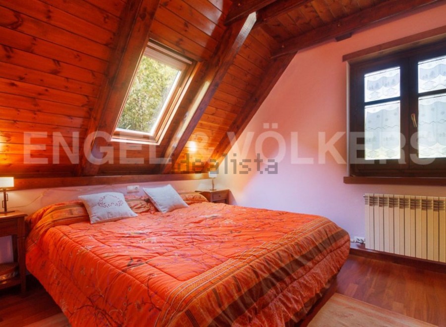 Cozy attic bedroom with wooden beams and skylights, offering abundant natural light.