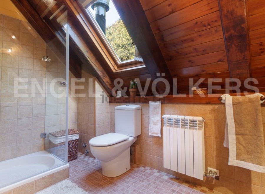 Charming attic bathroom with skylight, wooden beams, and tiled walls.