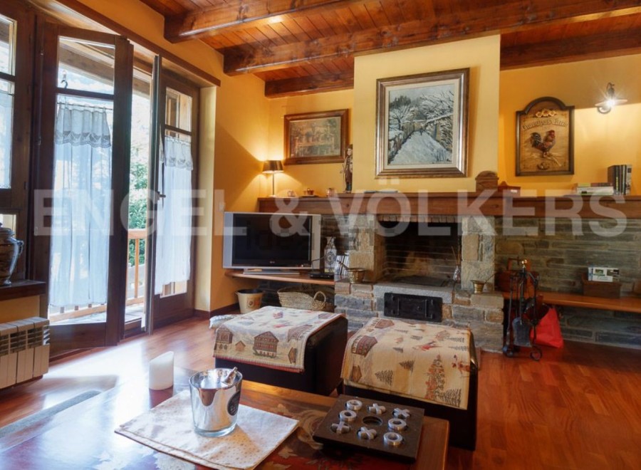 Cozy mountain chalet with a stone fireplace, hardwood floors, and large windows offering scenic views.
