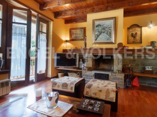 Cozy mountain chalet with a stone fireplace, hardwood floors, and large windows offering scenic views.