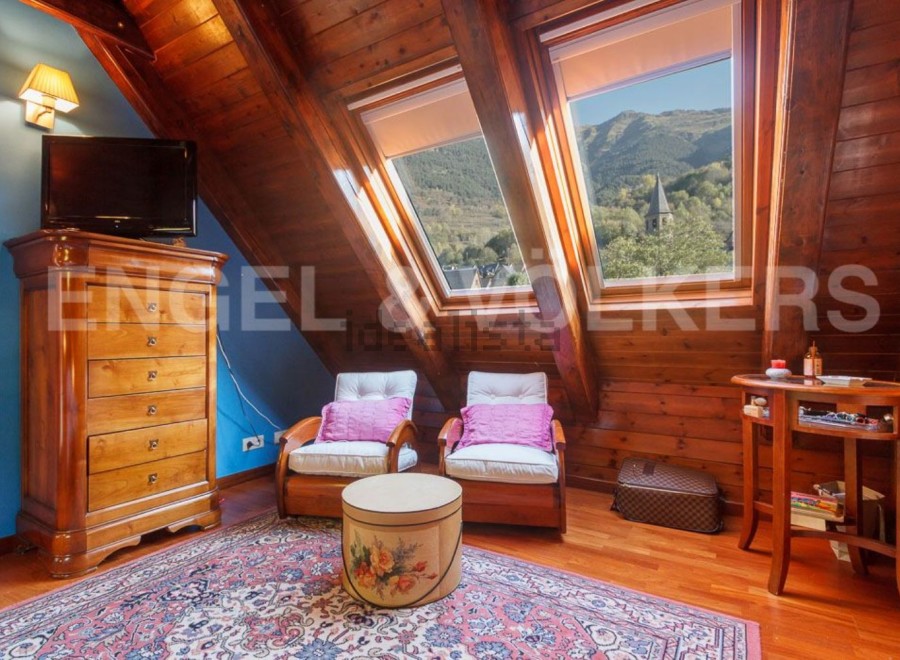 Charming attic bedroom with wooden beams, skylights offering mountain views, and a cozy sitting area.