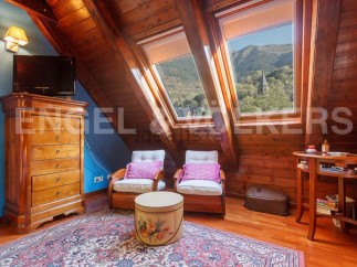 Charming attic bedroom with wooden beams, skylights offering mountain views, and a cozy sitting area.