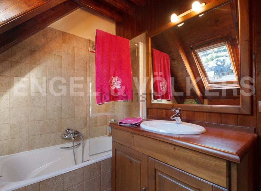 Charming attic bathroom with wooden beams, a bathtub, and a vanity with a wooden countertop.