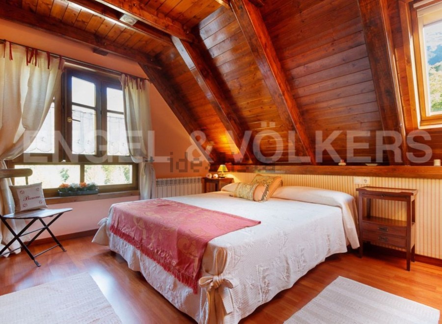 Cozy attic bedroom with wooden beams and large windows offering stunning views.