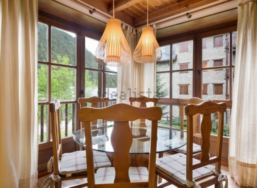 Charming wooden dining area with glass-top table and comfortable seating, bathed in natural light from large windows offering scenic mountain views.
