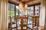 Charming wooden dining area with glass-top table and comfortable seating, bathed in natural light from large windows offering scenic mountain views.