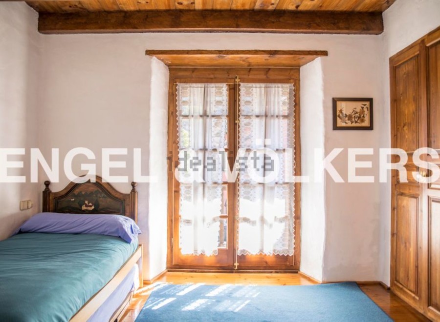 Charming rustic bedroom with wooden beams and floors, featuring a single bed and large window with lace curtains.