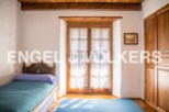 Charming rustic bedroom with wooden beams and floors, featuring a single bed and large window with lace curtains.