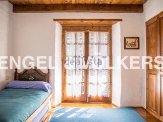 Charming rustic bedroom with wooden beams and floors, featuring a single bed and large window with lace curtains.