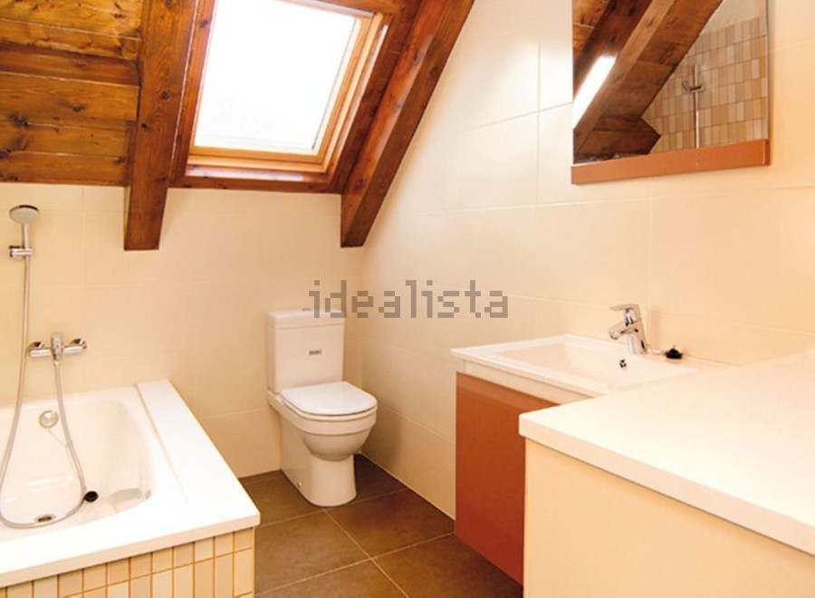 Charming attic bathroom with wooden beams, skylight, and modern fixtures.