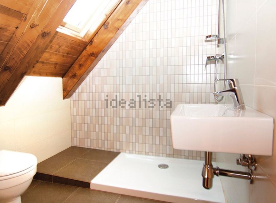 Charming attic bathroom with wooden beams, skylight, and modern fixtures.