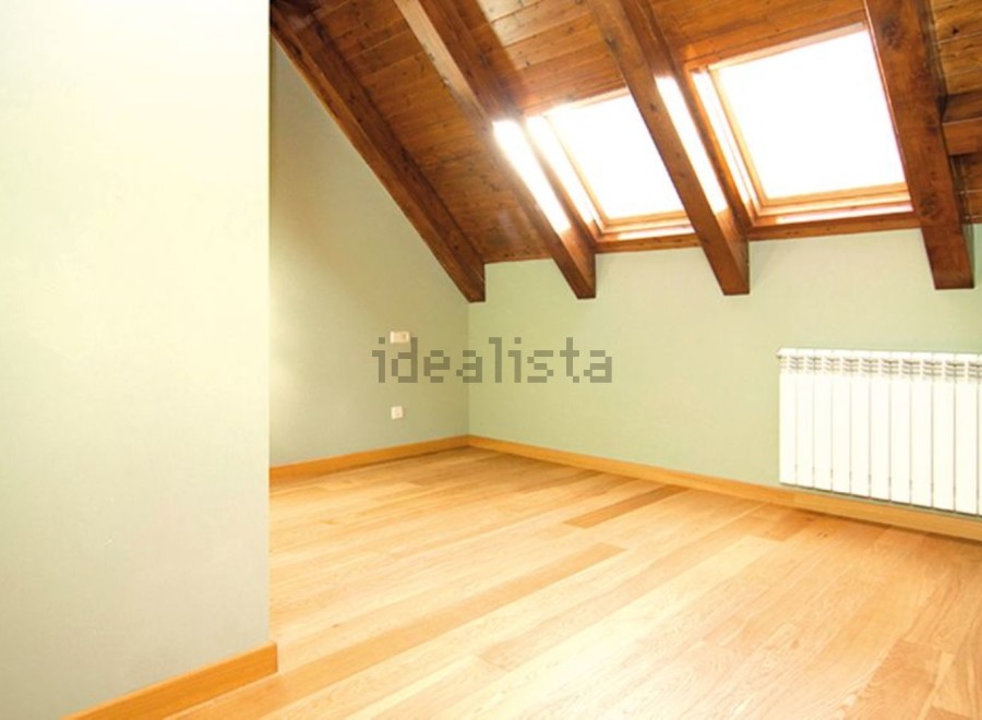 Bright attic room with wooden beams and skylights.