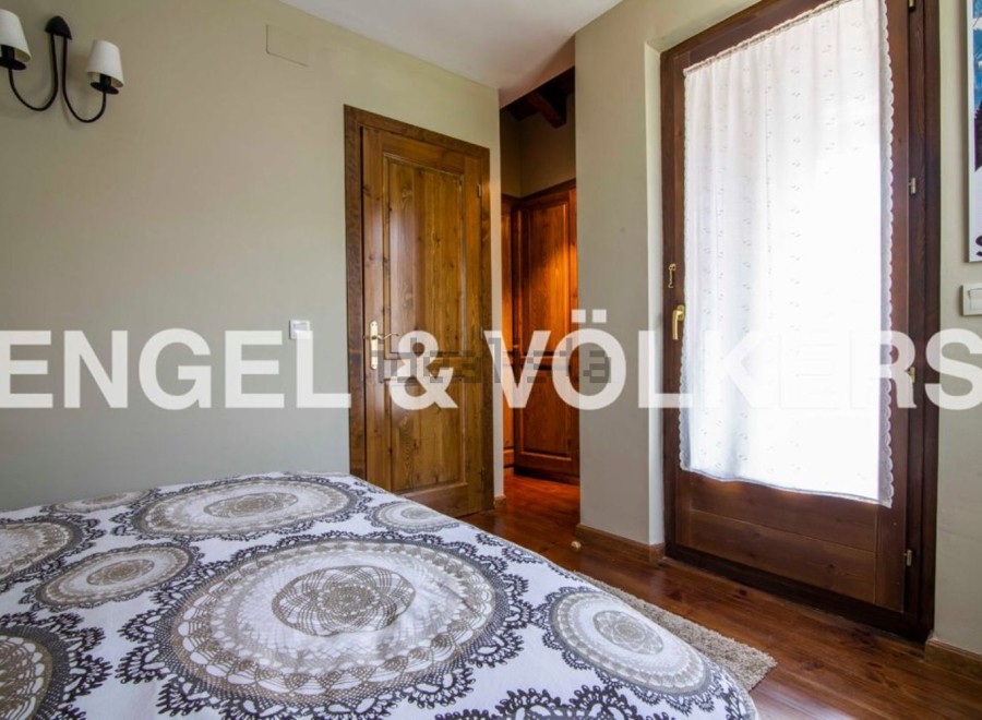 This charming bedroom boasts a cozy and elegant atmosphere, featuring a comfortable bed with a beautiful patterned duvet and a wooden door leading to a spacious closet.