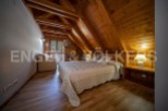 Cozy attic bedroom with wooden beams and flooring, featuring a comfortable double bed and a small sitting area.