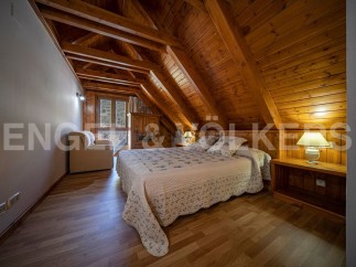 Cozy attic bedroom with wooden beams and flooring, featuring a comfortable double bed and a small sitting area.