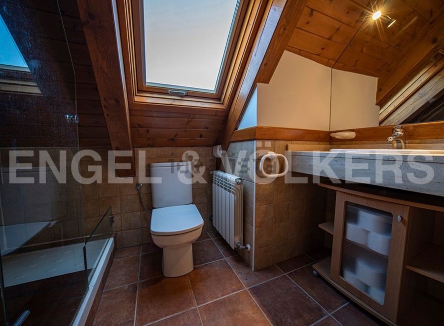 Charming attic bathroom with skylight, wooden beams, and a modern toilet and sink.